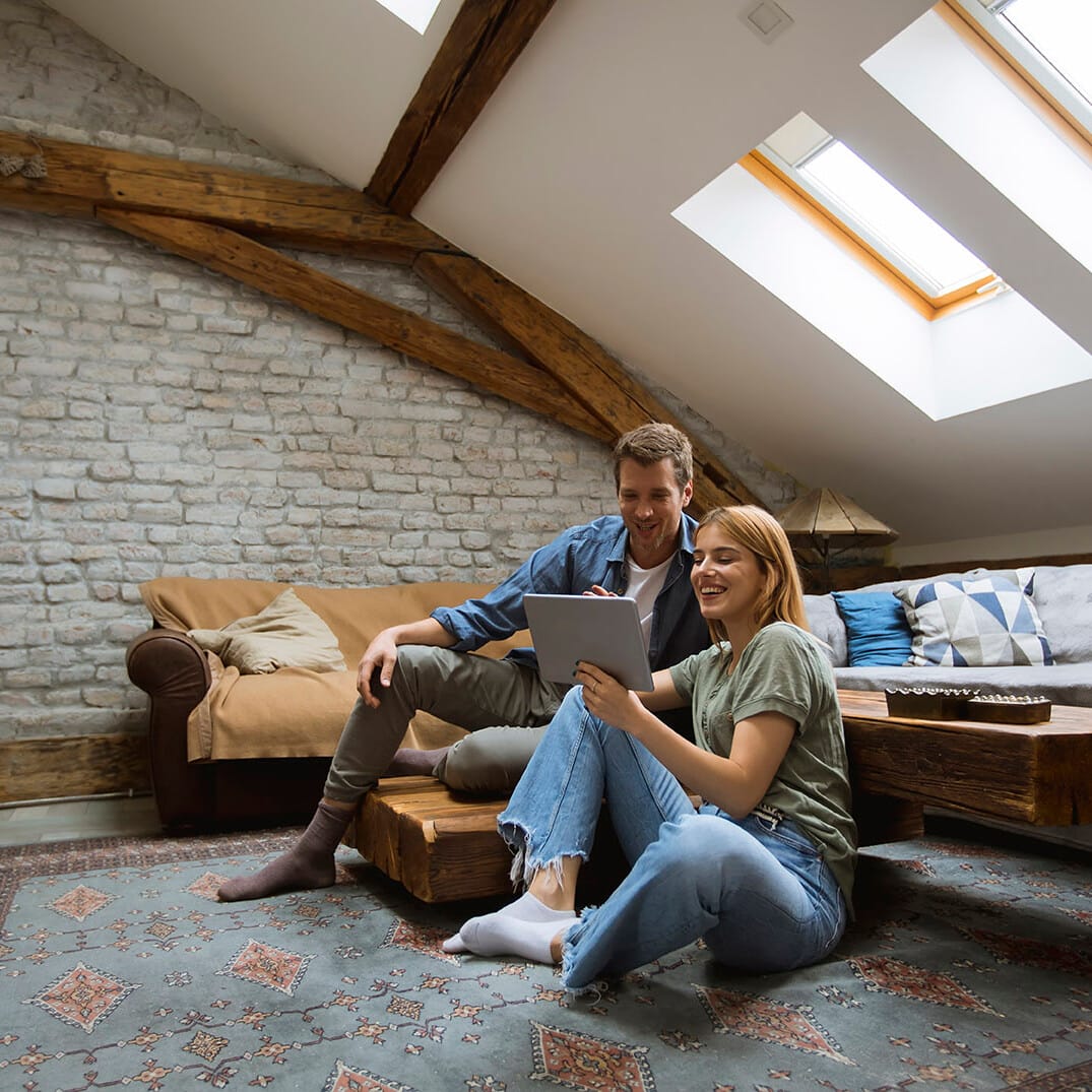 Image shows a couple sitting on the floor of a loft room. Image depicts loft conversions in Hitchin